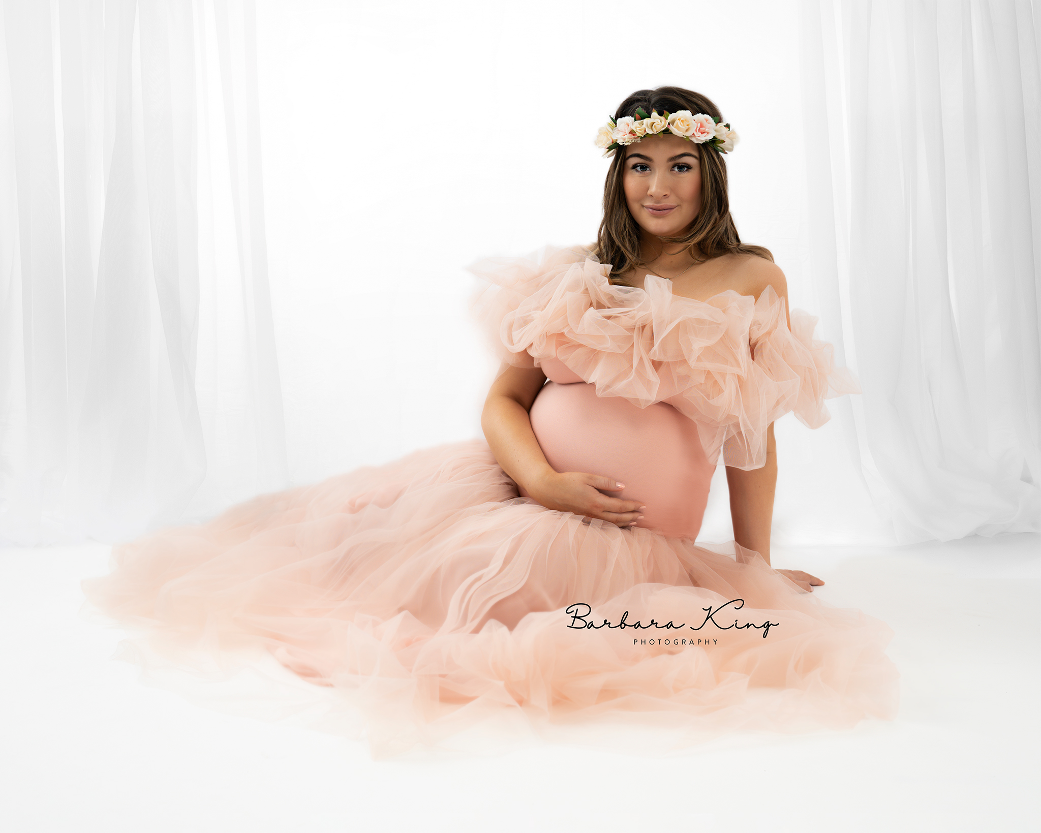 pregnant lady sitting on floor in pink dress with flowers in her hair